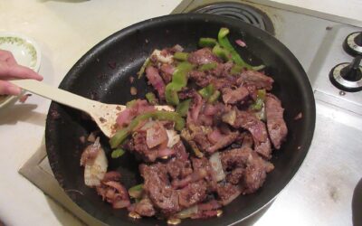 Carne e legumes sendo refogados numa frigideira antiaderente sobre o fogão